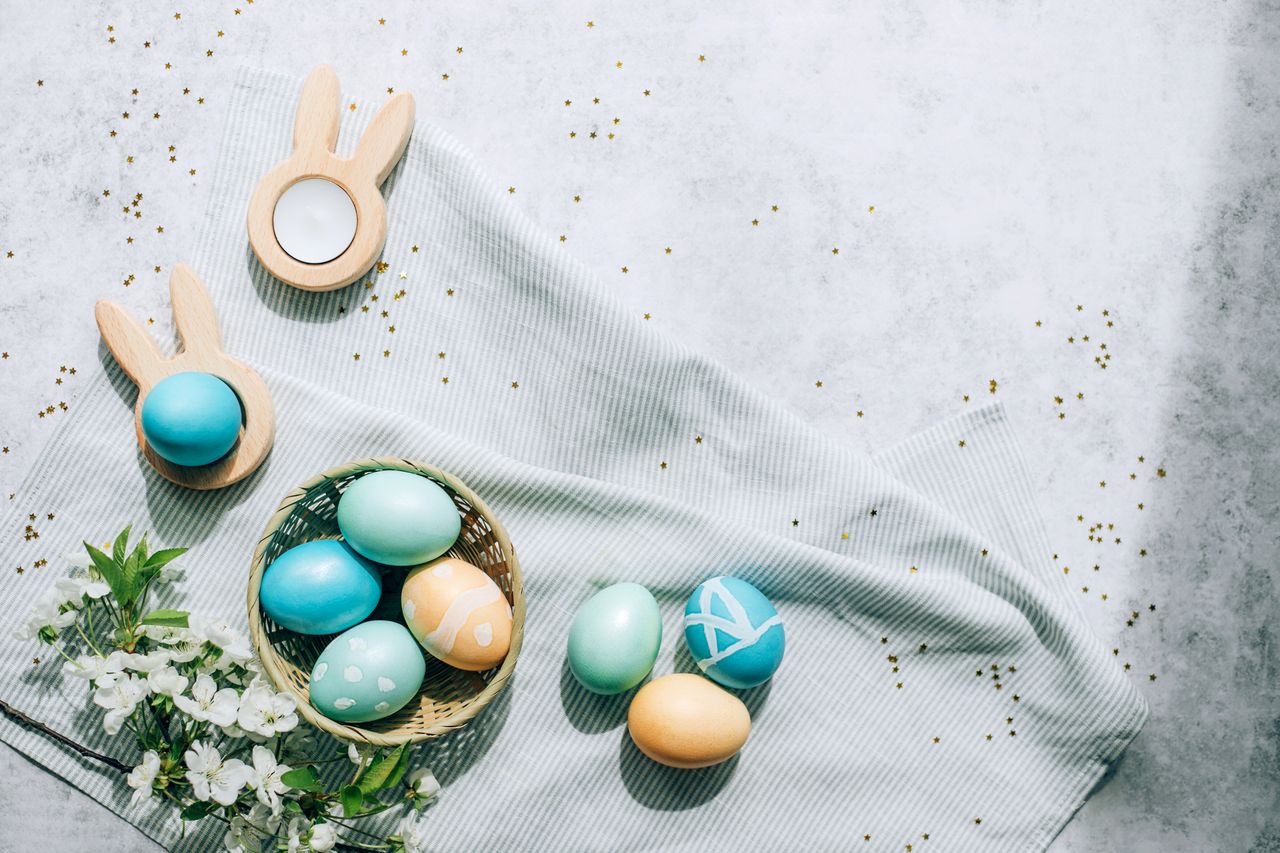 A grey table cloth decorated with blue and cream easter eggs and a bunch of flowers.