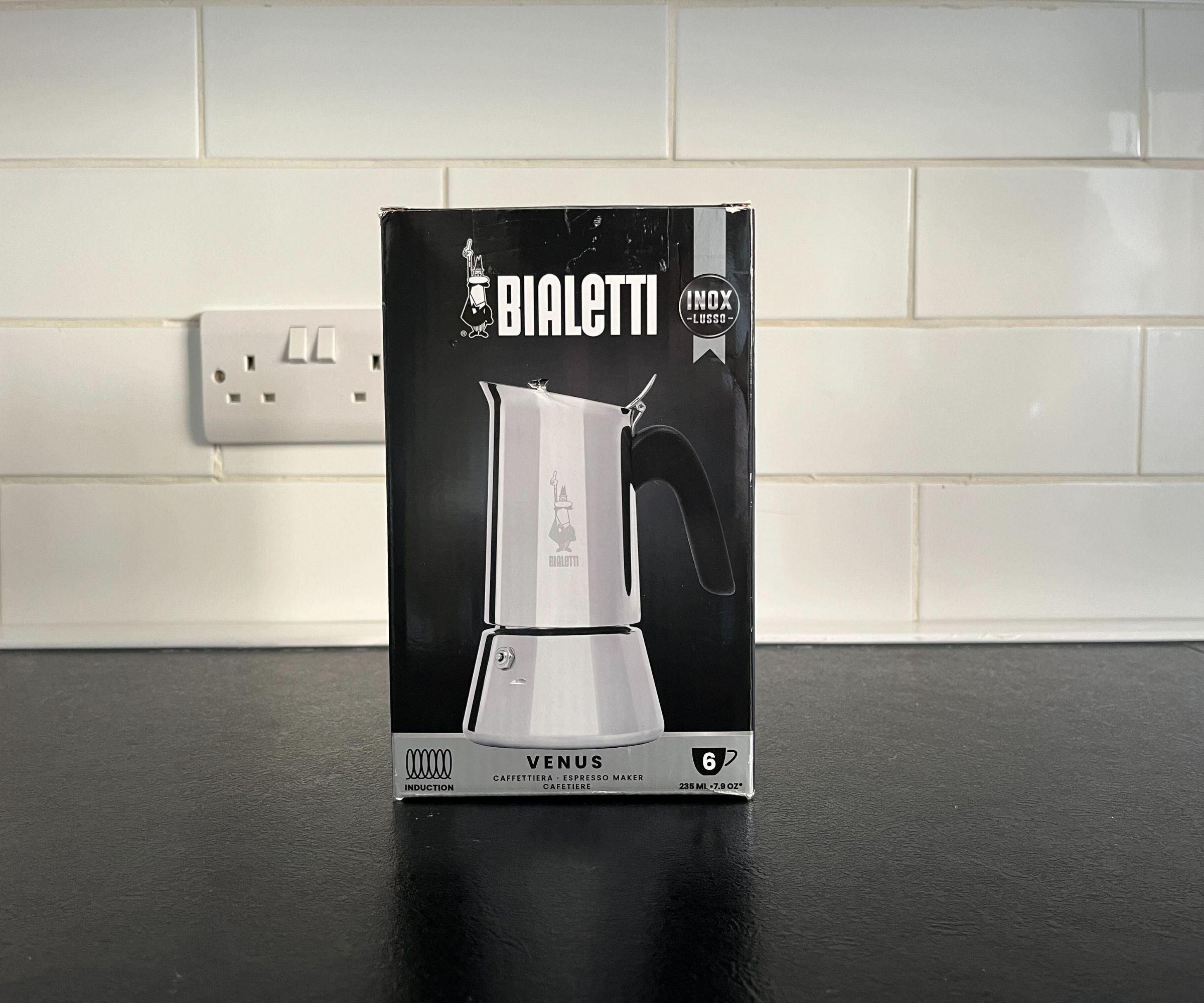 The Bialetti Venus coffee maker box on a black counter, with a white tile backsplash behind