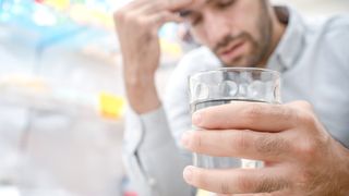 man suffering from chronic pain holding a glass of water