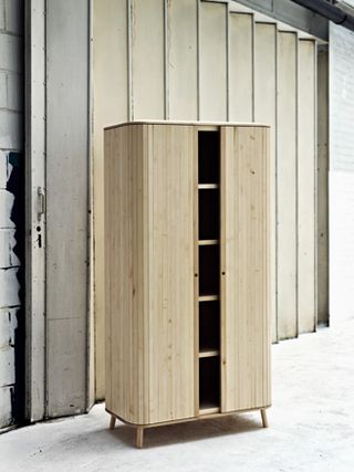 Wooden Cabinet with a peek of the interior showing 5 shelf layers. Photographed on a grey concrete floor against a metal slding gate/exit