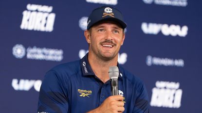 Bryson DeChambeau speaking into a microphone at his LIV Golf Korea press conference