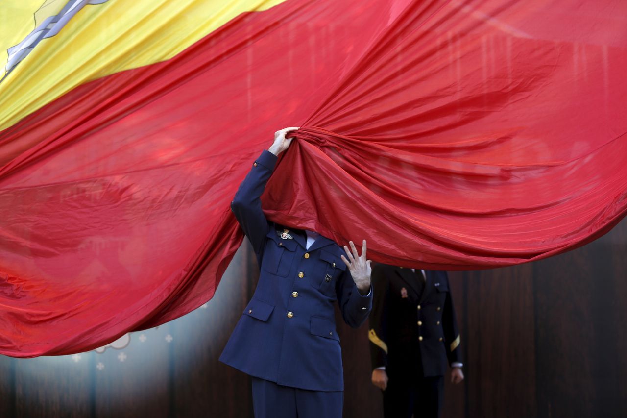 A member of the Spanish Armed Forces gets his face covered by a giant Spanish flag as he helps raise it during a ceremony to mark the 37th anniversary of the 1978 Spanish constitution in Madr