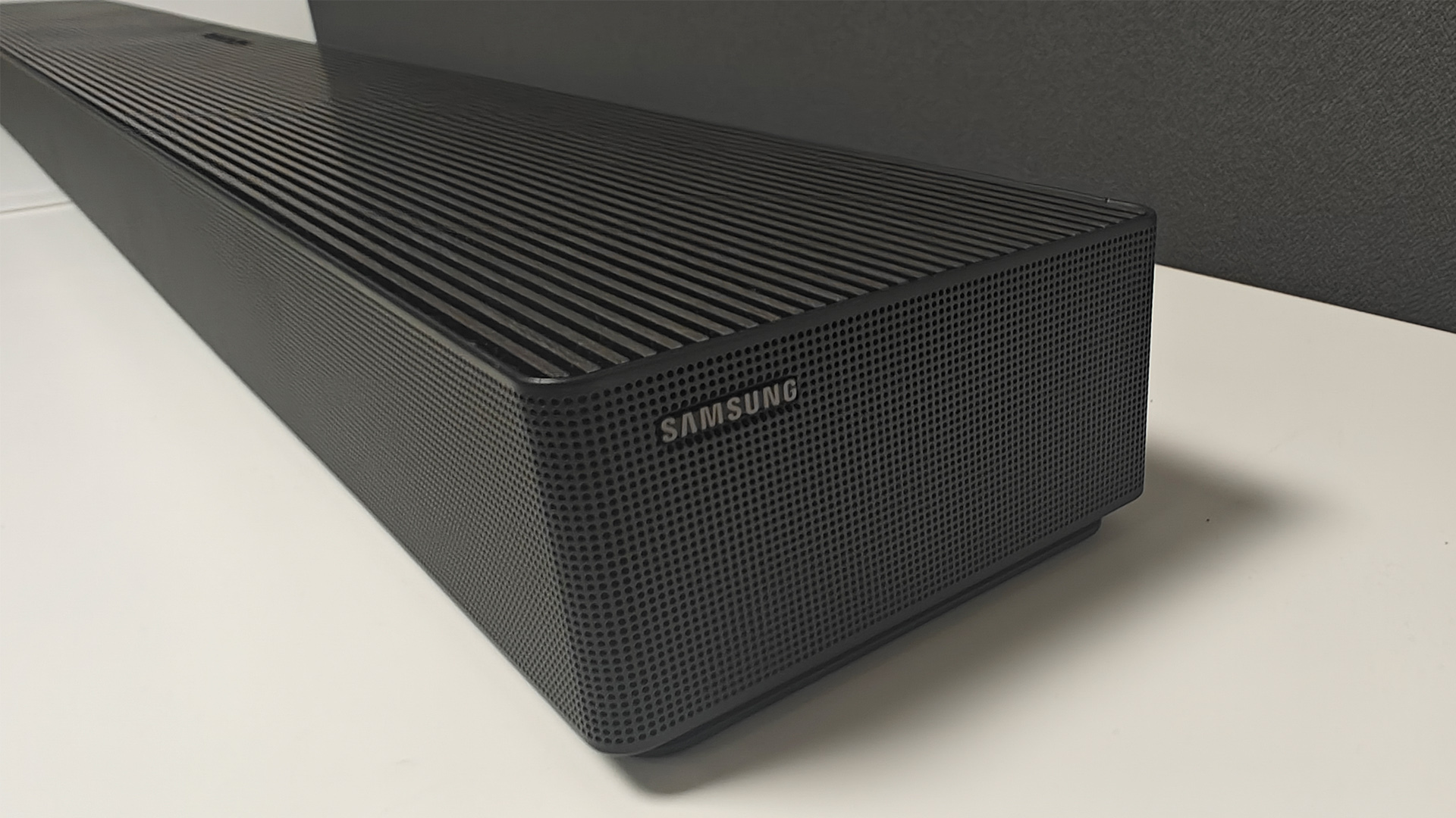Samsung HW-QS90H Dolby Atmos soundbar on white shelving unit end of unit showing Samsung logo