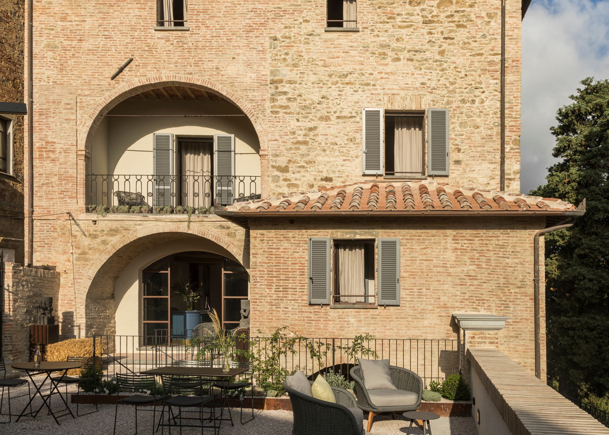 An Italian hotel with arched balconies, blue wood shutters, bistro furniture, and a tiled roof