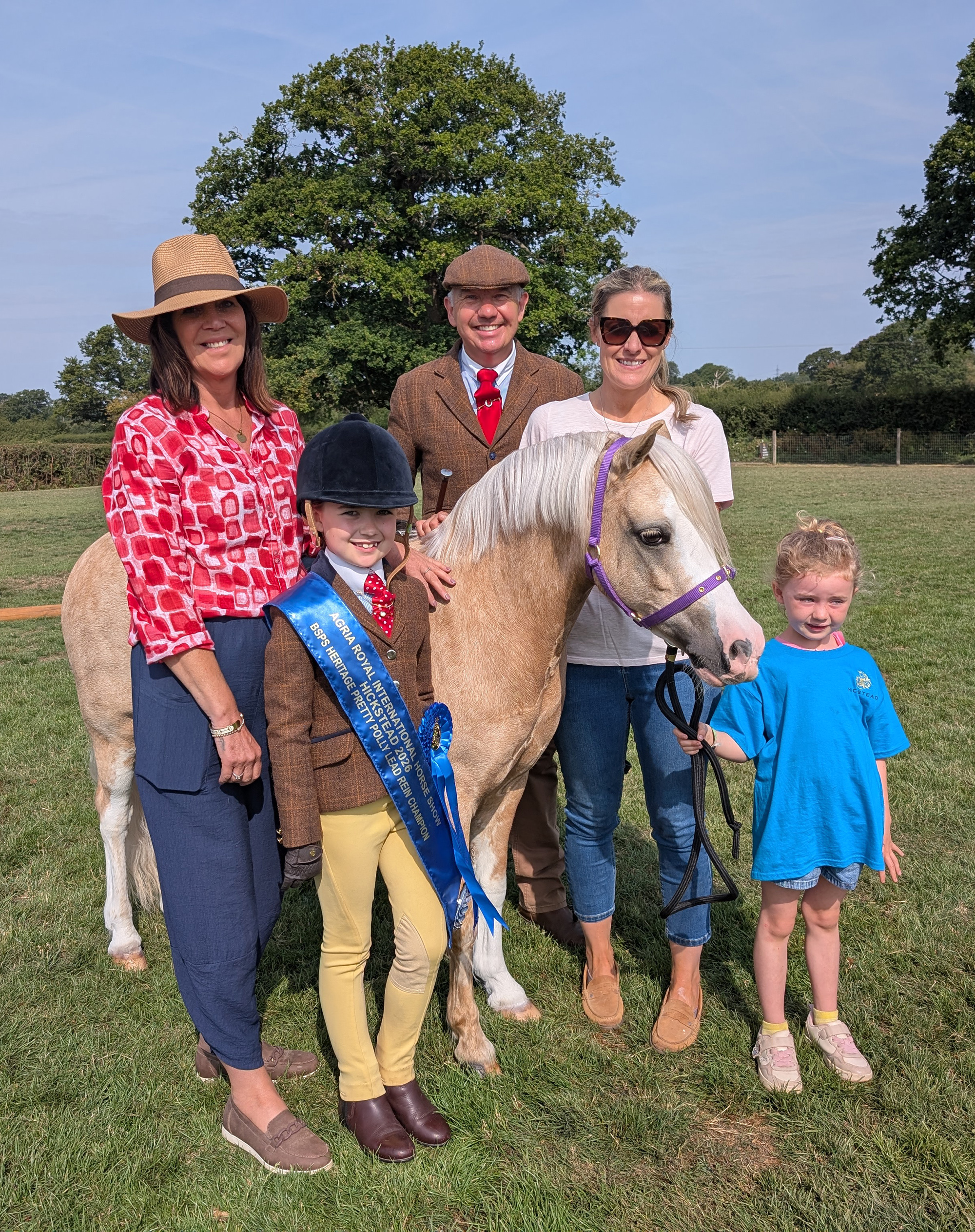 A palomino pony wearing a headcollar is surrounded by her family including young female rider wearing her blue winner&amp;rsquo;s sash and rosette