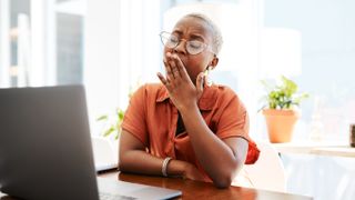 Why do I feel sleepy after eating? Image shows young woman yawning at desk