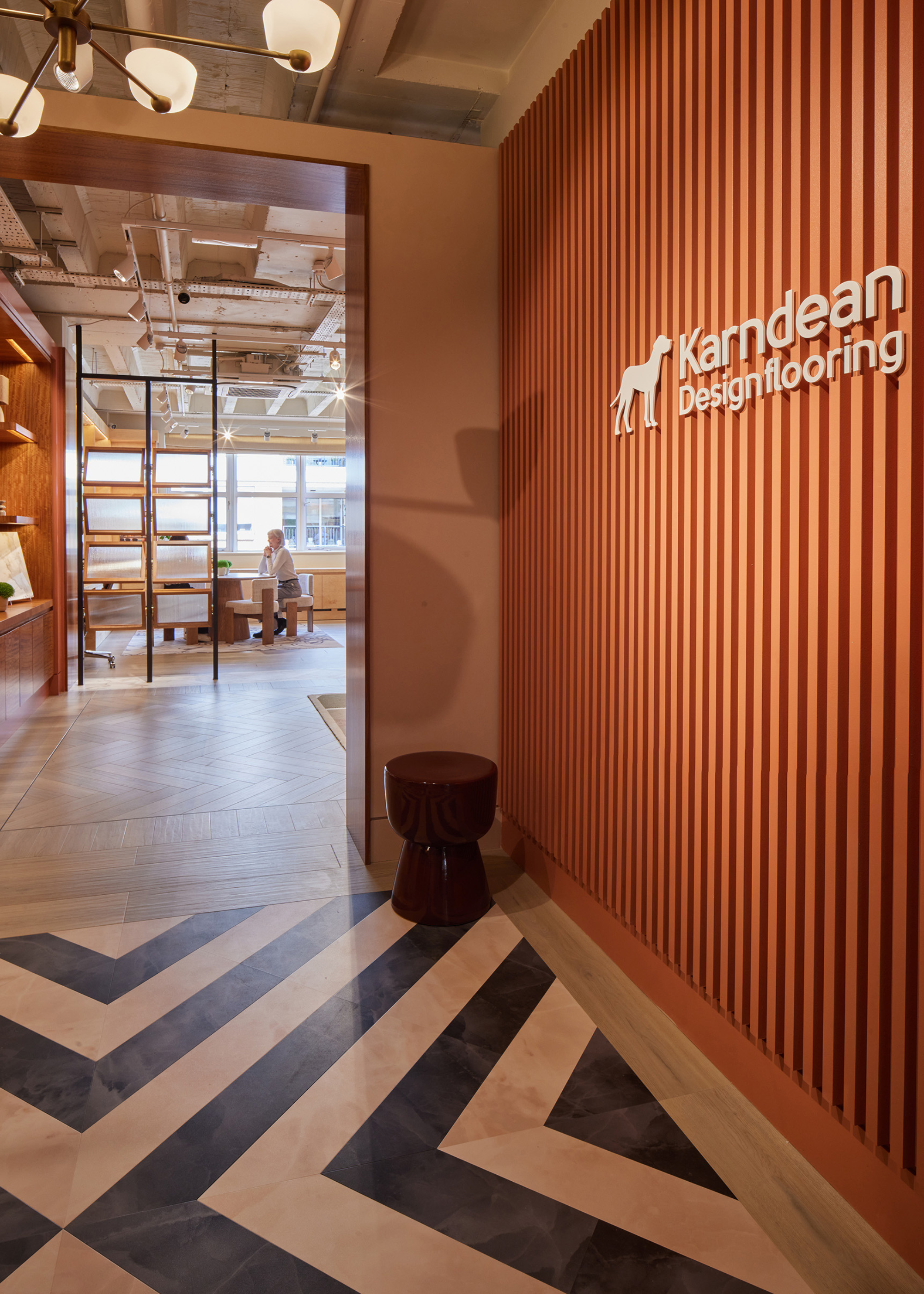 An entrance to a showroom with tile flooring, a single stool, and a panelled wall with a logo