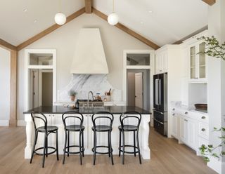 farmhouse kitchen with white island with black top and black bar chairs
