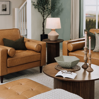 living room with brown leather armchair and sofa with cushions on, next to coffee table