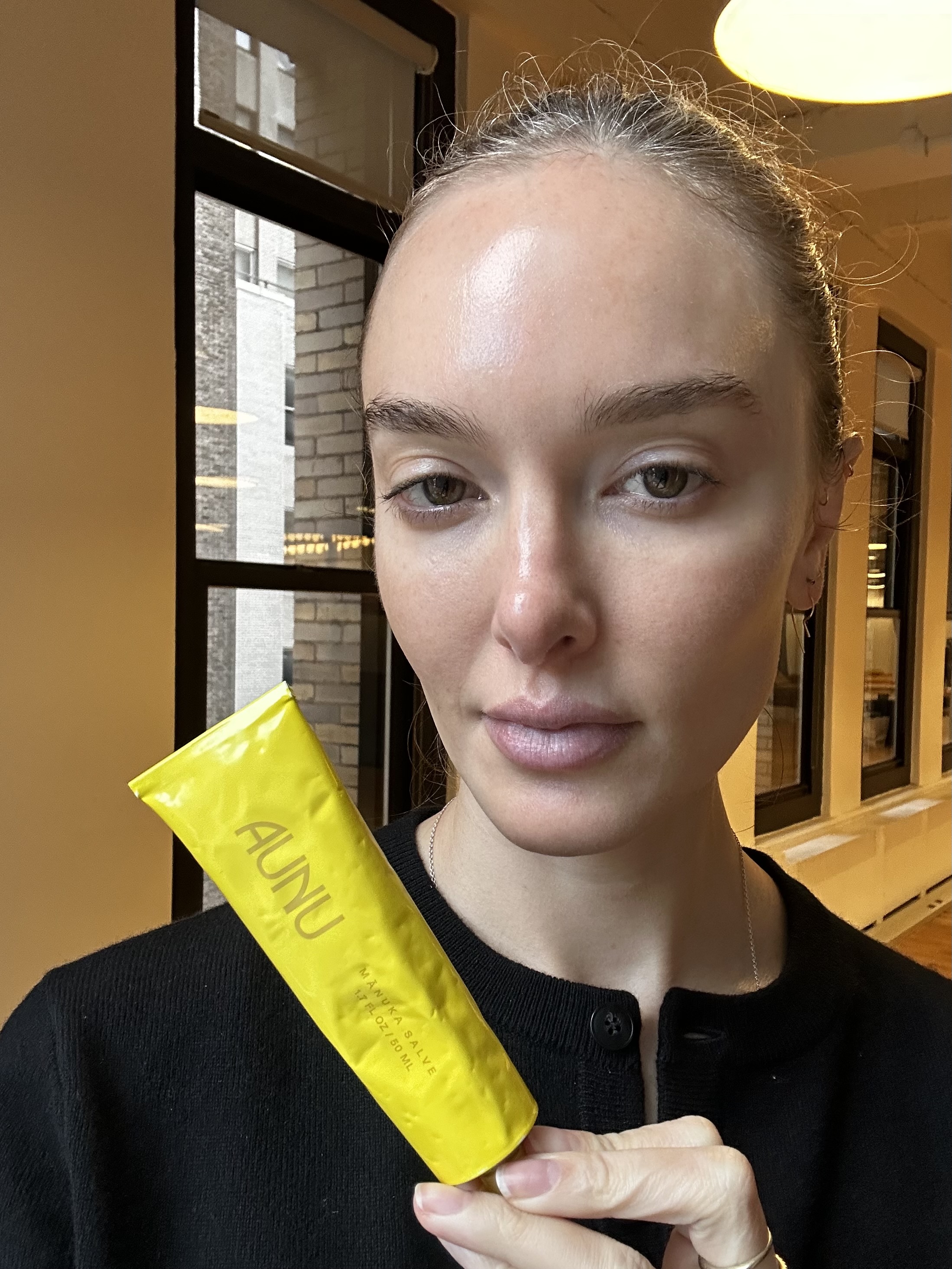 a woman in a black sweater holding a yellow tube of Aunu skincare