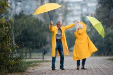 Happy mature couple with umbrellas having fun while dancing during rainy day in the park. Copy space.