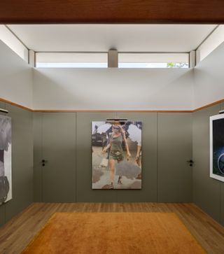 Wall art inside Ventana House in Mexico, wood flooring, wall lights, large orange floor rug, grey/green walls, two doors built into the wall with black door handles, white ceiling with skylight windows