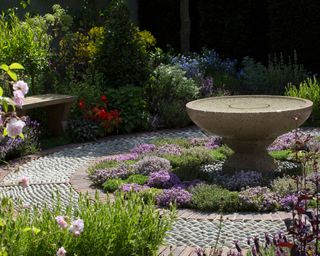 stone bird bath in a cobbled terrace area surrounded by lavender and herbs and other
