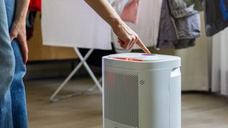 Person crouching down to touch a button on a dehumidifier in front of laundry hung up