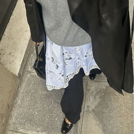 A woman wearing a minimalist outfit, with a white skirt and black coat