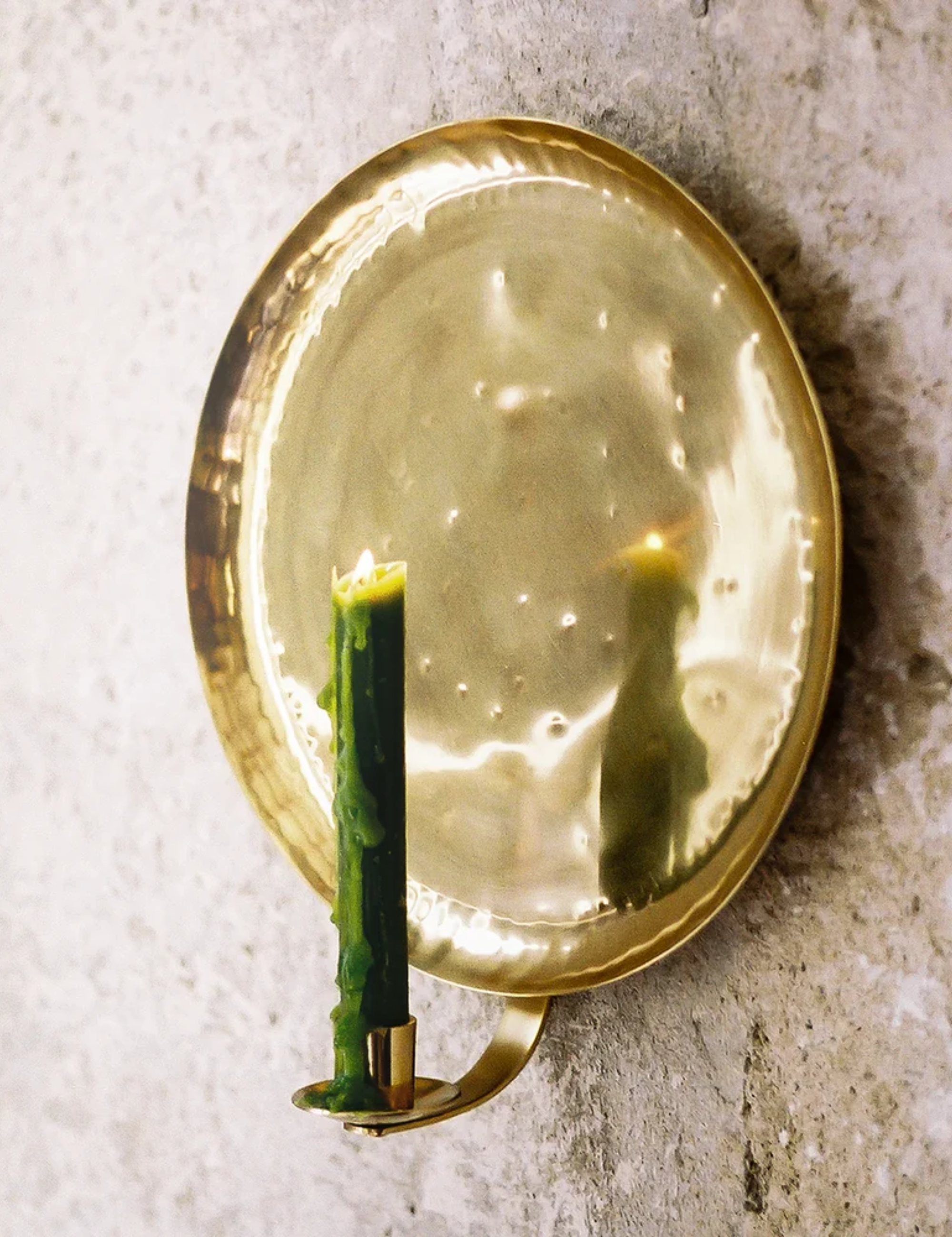 Pooky's Bellamy Candle Sconce styled with a lit moss green taper candle against a textured exterior wall