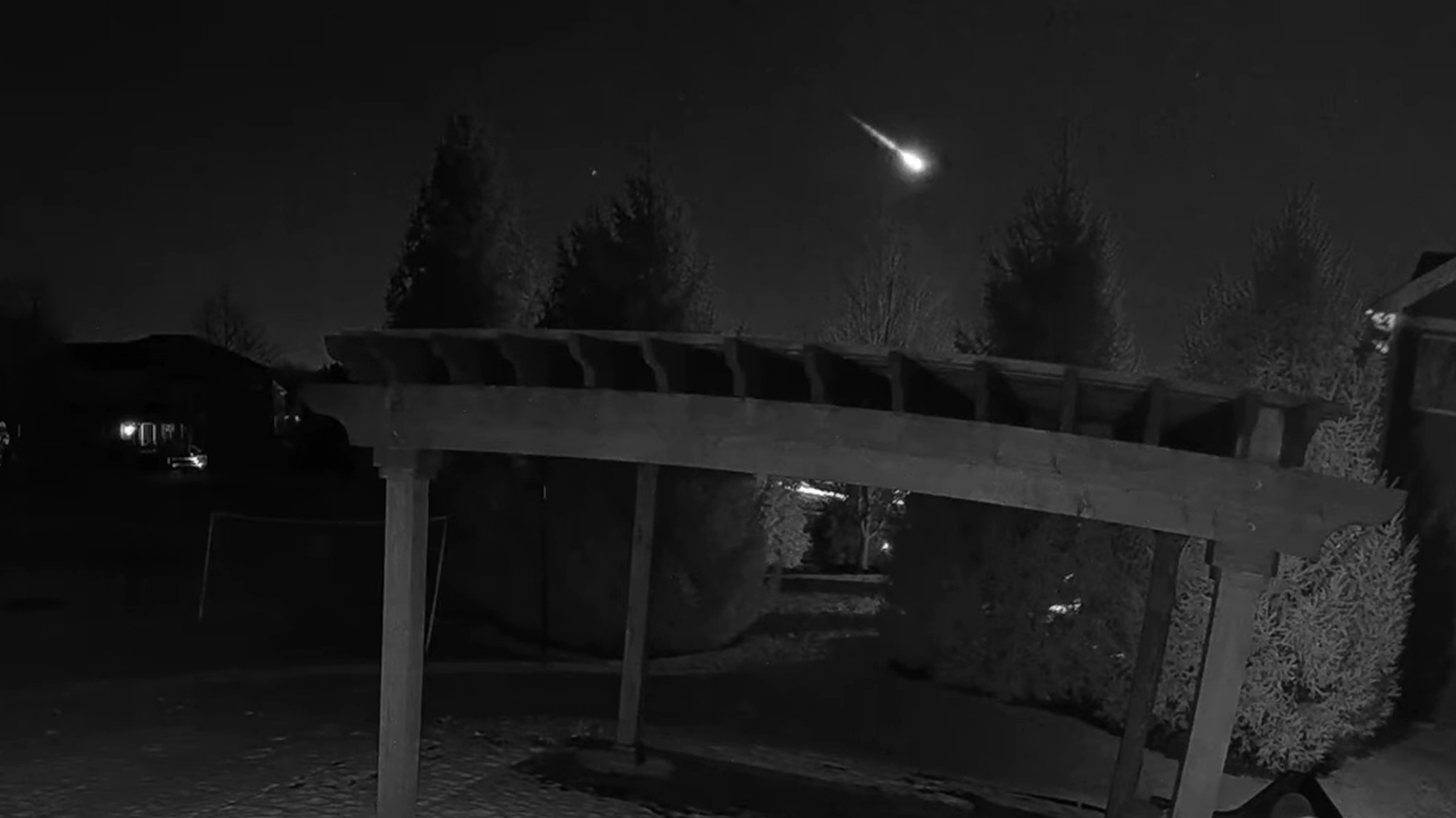 A fireball is captured streaking through the night sky above an awning, with trees in the background.
