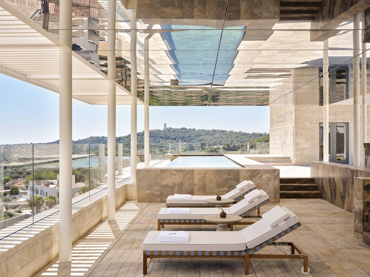 A design hotel with historic, vaulted architectural walls houses a selection of retro-inspired furniture, including colorful sculptural armchairs, layered wallpapers and panels, tiled flooring, eye-catching artworks, and wavy sofas, along with a panoramic rooftop bar with sun loungers.