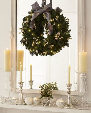 White mantelpiece with candles and glass decorations and a hanging wreath