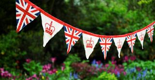 Royal-theme bunting with crowns and Union Jacks hanging in a garden for a coronation decoration idea