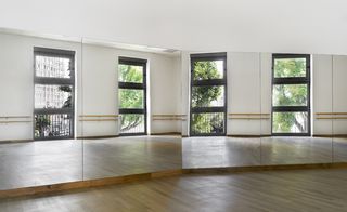 Interior room at the Lilas Animation Centre in Paris, wooden floor, mirrored wall, white ceiling, bllack framed windows reflected in the mirrors, with view of surrounding buildings and trees
