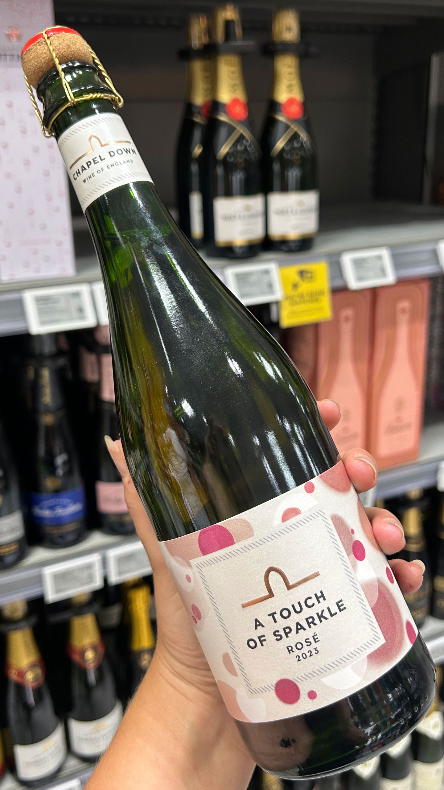 A hand holding a bottle of Chapel Down, A Touch of Sparkle Ros&amp;eacute; 2023 wine in a supermarket