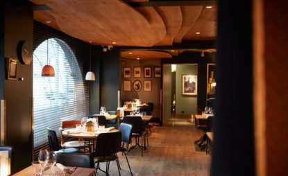 Dining area with wooden tables and dark, leather chairs below a stepped, wooden ceiling