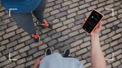 Woman holding phone with fitness chart that reveals what does running do to your body, wearing running shoes standing next to friend with running shoes on