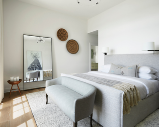 Greige minimal bedroom with large floor mirror, four poster bed and wooden round wall art pieces