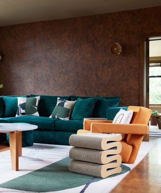 A living room with textured brown walls, a white and green area rug, a dark green sofa and a sculptural, whimsical side table