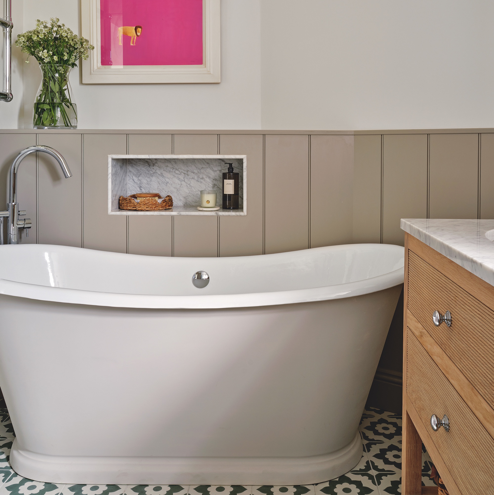 large freestanding slipper bath in bathroom with wooden tone and groove panelling and patterned floor tiles, with pink artwork above bath and wooden vanity unit with marble top