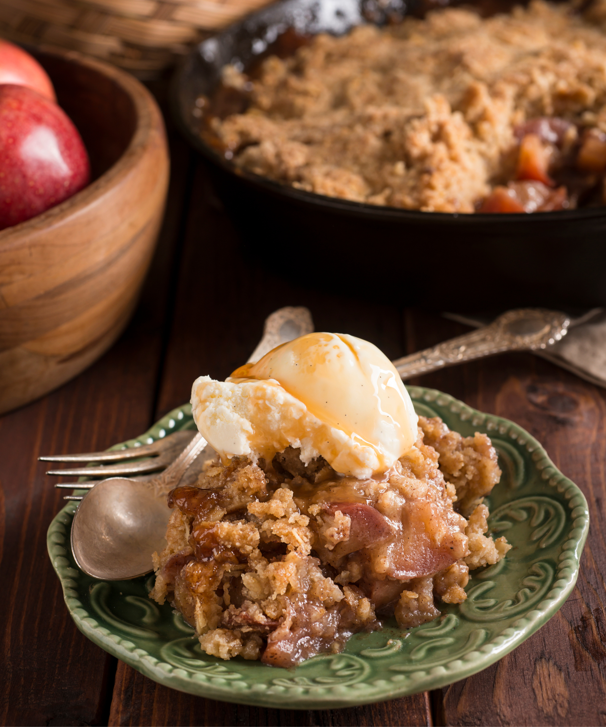 A portion of Skillet Apple Crisp served on a vintage plate, with the skillet in the background