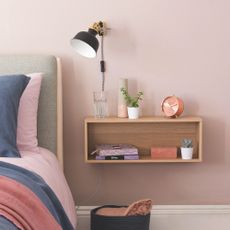 A wooden floating bedside table mounted on a pink wall with storage