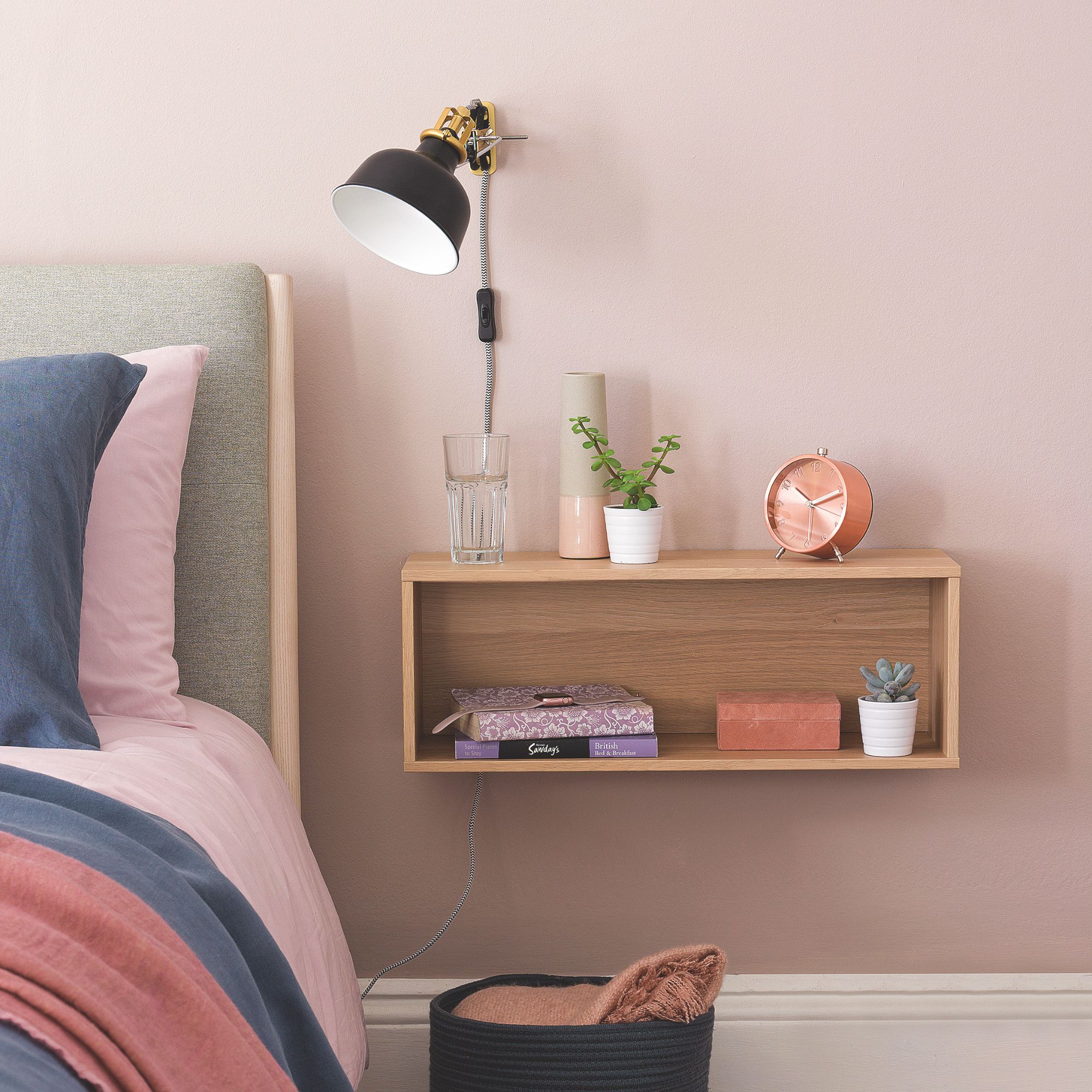 A wooden floating bedside table mounted on a pink wall with storage