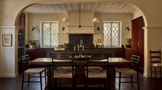 Open plan kitchen and diner with red cabinets and cream walls with dark countertop and a dark wooden island
