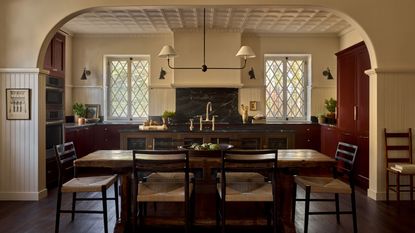 Open plan kitchen and diner with red cabinets and cream walls with dark countertop and a dark wooden island