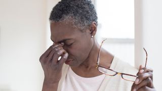Mature woman with tension headache holding glasses.