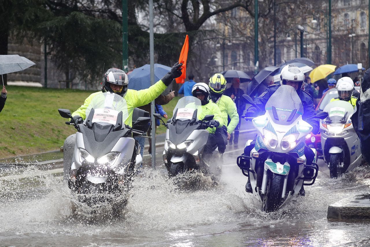 The lead motorcycles warn riders of puddles at the start of Milan-San Remo