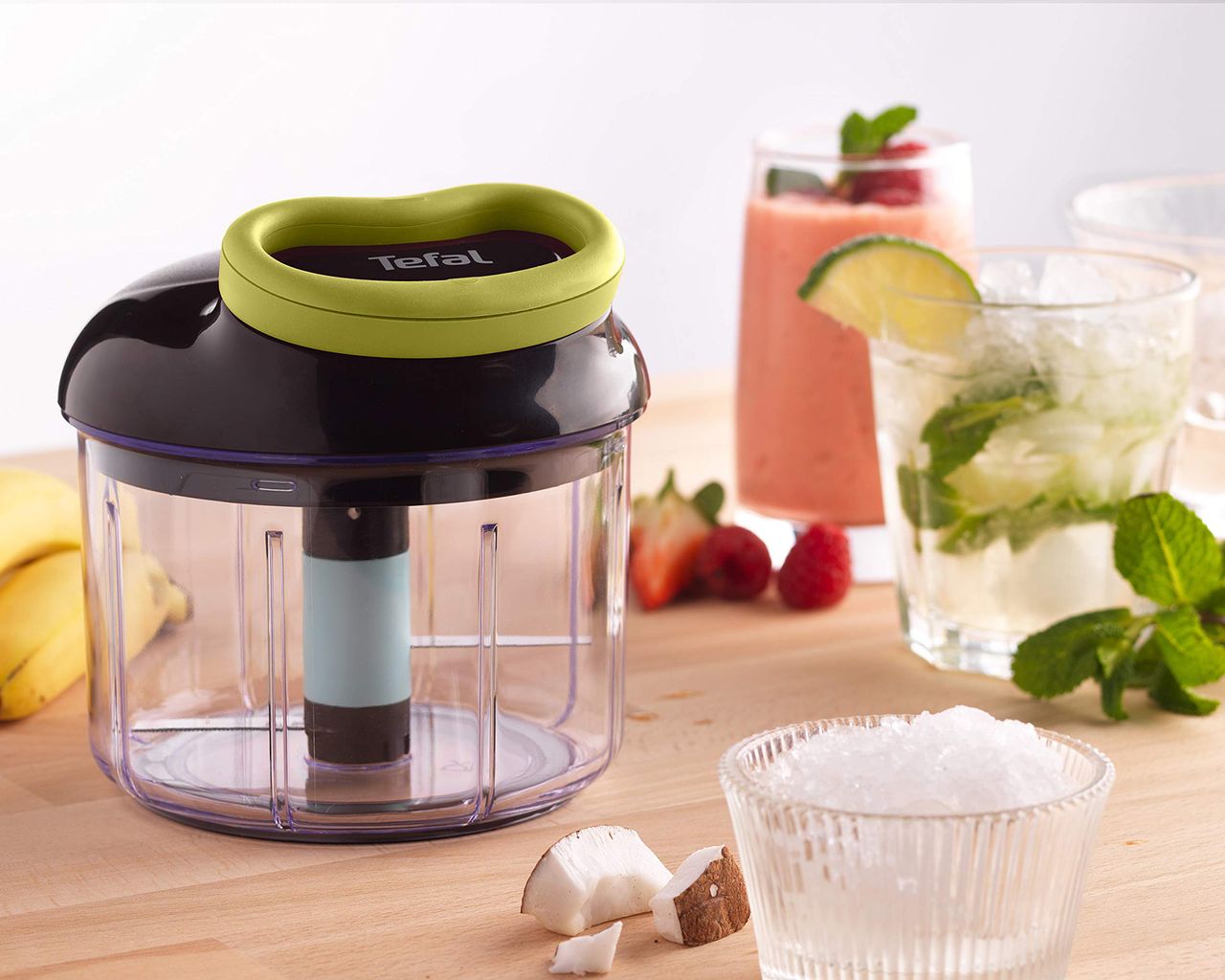 Tefal black and green manual chopper in kitchen with fruit smoothie, desiccated coconut and carbonated drink with mint and lime