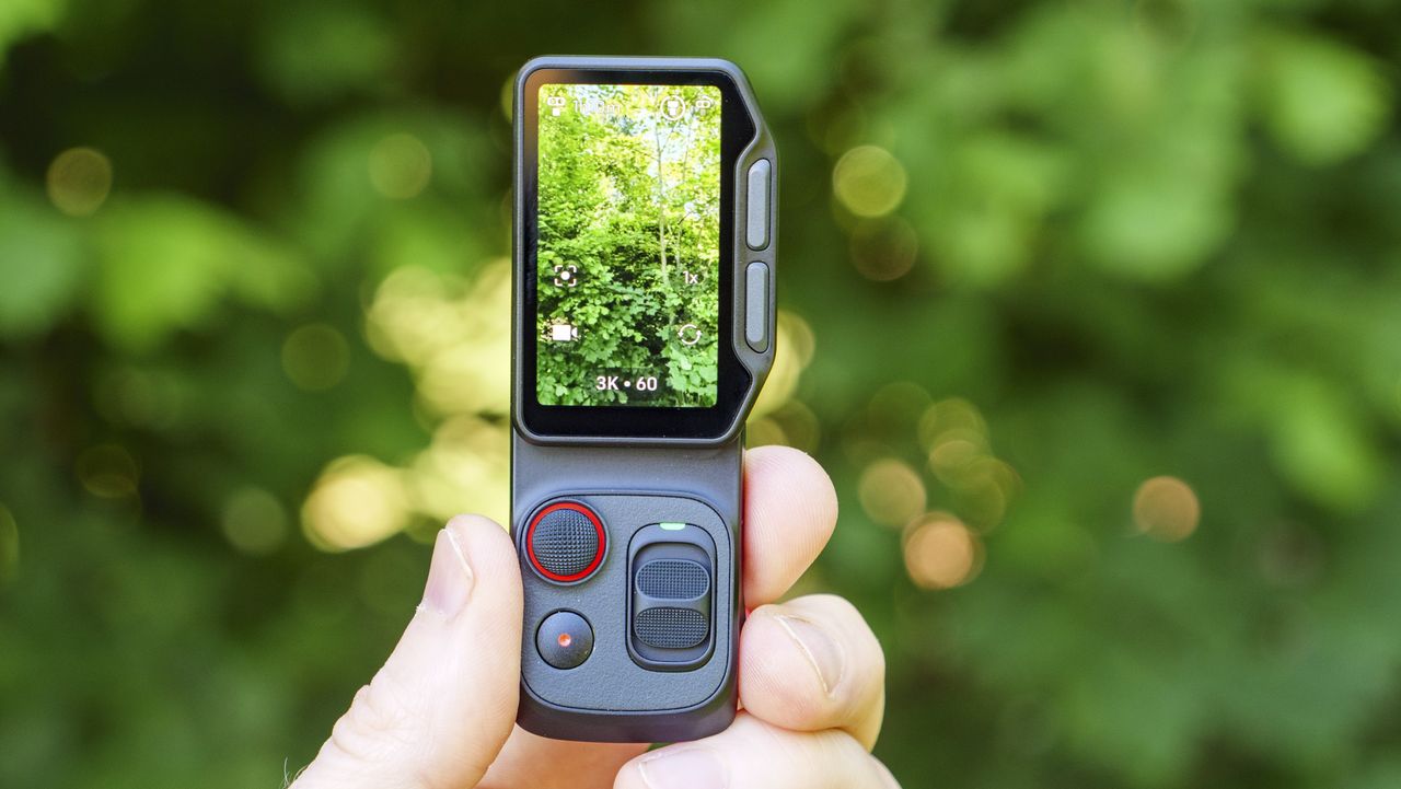 Closeup of the Insta360 Luna Ultra vlogging camera's detachable monitor in person's hand, leafy background, screen in vertical format