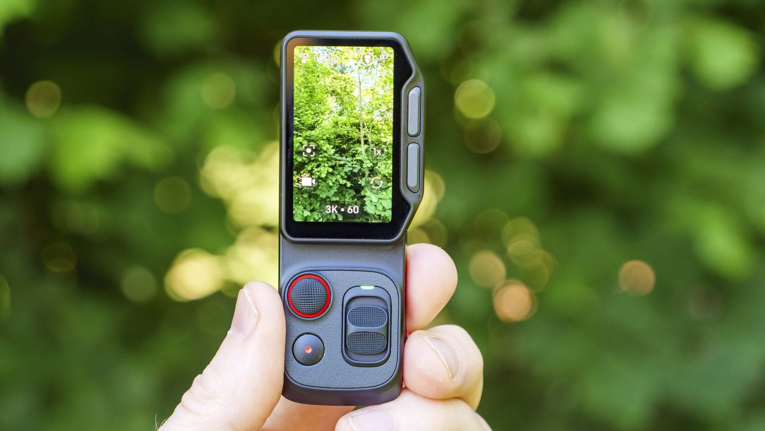 Closeup of the Insta360 Luna Ultra vlogging camera's detachable monitor in person's hand, leafy background, screen in vertical format