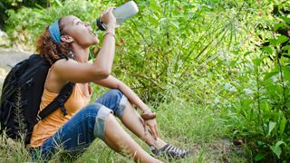 A woman hiking sat on the grass drinking her water