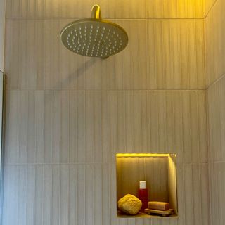 shower with neutral tiles and brass shower head and storage alcove for toiletries