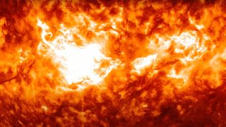 closeup of a bright flash of white light erupting on the sun's orange surface