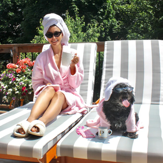 Woman and dog wearing matching pink bathrobes and sunglasses, sitting on stripy sunloungers