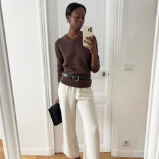 French influencer wearing a brown sweater, silky white pants, and a leather belt