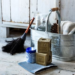 Metal cleaning bucket with cleaning products and tools inside of it and next to it