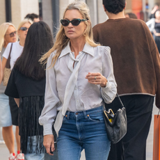 Kate moss wears sunglasses with a button-down shirt, bootcut jeans, and a black bag.
