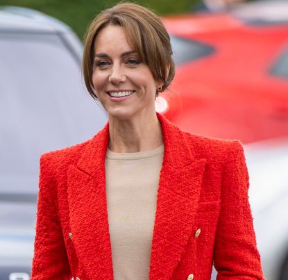 Kate Middleton wearing a red blazer and tan sweater smiling