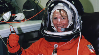 astronaut in a spacesuit and helmet gives the thumbs-up
